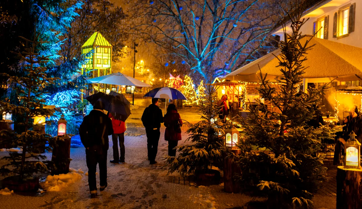 Mit Schnee sieht der ganze Lichterzauber gleich noch viel schöner aus. Menschen spazieren in einer beleuchteten Winterlandschaft.